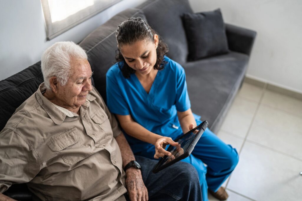 Home Caregiver showing tablet to senior man at his house
