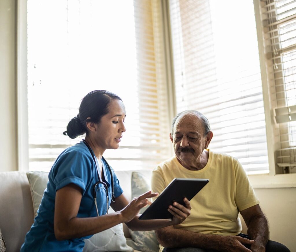 Mid adult nurse using digital tablet while talking to a senior man in a consultation in the living room of a nursing home